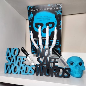 May include: A book titled "Nights" with a skeleton hand and a skull design. The words "No Safe Words" are displayed in blue and black 3D lettering, along with two toy knives and a blue skull.