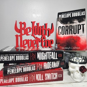 May include: A stack of three books by Penelope Douglas, including "Nightfall", "Hideaway", and "Kill Switch", with a red decorative sign that reads "Be with Never live". A copy of "Corrupt" is also visible.