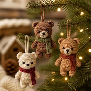 Peut inclure: Trois ours en crochet suspendus à un sapin. Un ours est crème avec une écharpe rouge foncé, un est marron moyen avec une écharpe rouille, et un est marron foncé avec une écharpe vert sauge. Chaque ours a des yeux noirs et un nez brodé.