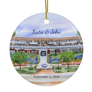 May include: A round ceramic ornament featuring a watercolor illustration of a multi-story building with balconies, surrounded by trees and flowers. The text Katie & John is printed above the building, and September 5, 2026 is printed below.