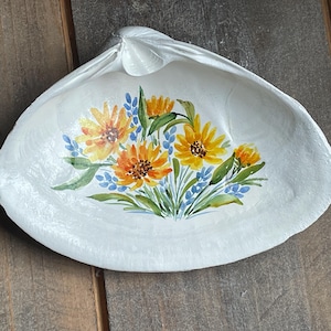 May include: A white seashell dish with a painted design of yellow and orange flowers with blue accents.