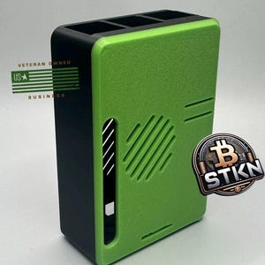May include: A green and black 3D printed case with a black vent and a sticker that says "STIKN" with a Bitcoin symbol. The case has the text "Veteran Owned US Business" on the side.
