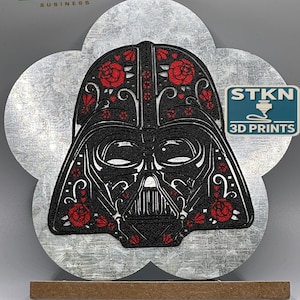 May include: A black and red 3D printed Darth Vader bust with a Day of the Dead inspired design. The bust is on a silver metal base with a wooden stand. The image also includes a logo for STKN 3D Prints.