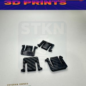 Puede incluir: Cuatro clips negros impresos en 3D, dos con un patrón de fibra de carbono, se muestran sobre una superficie blanca. La imagen incluye el texto "STKN 3D PRINTS" en una fuente retro y un gráfico "Veteran Owned US Business".