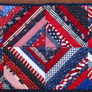 May include: A patriotic table runner featuring a patchwork design with red, white, and blue fabrics. The runner showcases diagonal stripes and geometric patterns, including stars and stripes, in a rectangular shape.