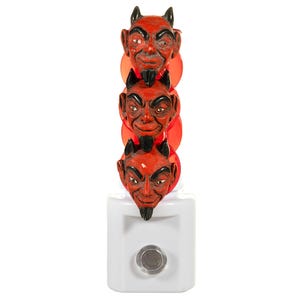 May include: A novelty night light featuring three red devil faces stacked vertically. Each face has black horns, a goatee, and a mischievous expression. The night light is mounted on a white base with a circular on/off switch.