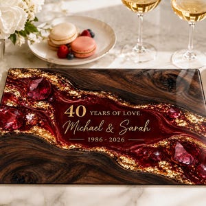 May include: A rectangular glass serving board featuring a dark wood grain pattern, a central deep red resin river, and gold leaf accents. The text reads 40 YEARS OF LOVE. Michael & Sarah 1986 - 2026 in white and gold lettering across the centre.