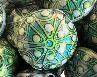 May include: A close-up of a pile of green and blue glass beads with a geometric pattern. The beads are iridescent and have a shiny finish.