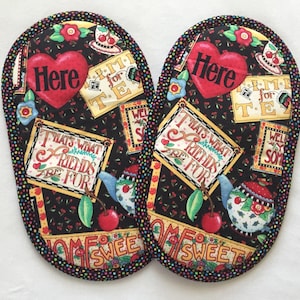 May include: Two black and white pot holders with a colorful floral pattern and the word "Here" in a red heart. The pot holders have a black and white polka dot trim.