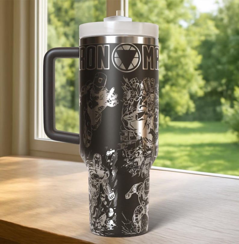 May include: Black stainless steel travel mug with a white lid and handle. The mug features a detailed silver graphic of Iron Man and the words "IRON MAN". The mug is designed to keep beverages hot or cold.