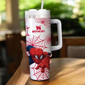 May include: White Stanley tumbler featuring Spider-Man. The tumbler has a red and white spiderweb design with the Spider-Man character in a dynamic pose. Includes a white handle and a straw.