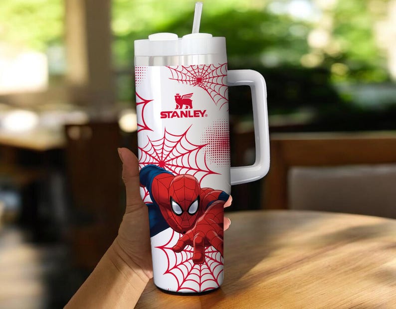 May include: White Stanley tumbler featuring Spider-Man. The tumbler has a red and white spiderweb design with the Spider-Man character in a dynamic pose. Includes a white handle and a straw.