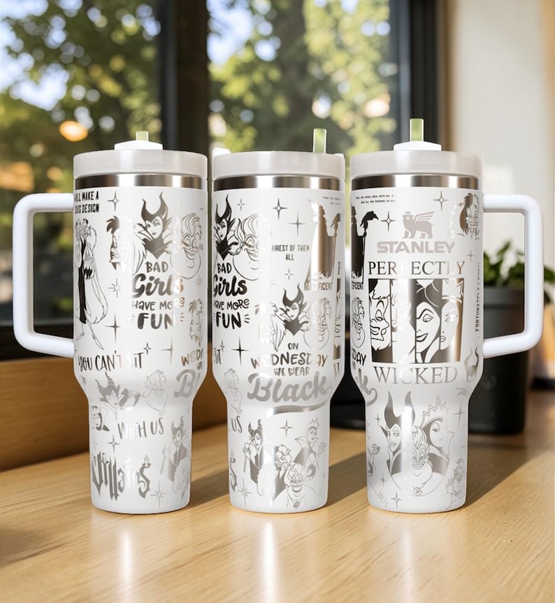 Puede incluir: Tres vasos aislados blancos con tapas y asas plateadas. Cada vaso presenta un dise&ntilde;o diferente con ilustraciones en negro y plata de personajes villanos y texto que dice "Bad Girls Have More Fun" y "On Wednesday We Wear Black".