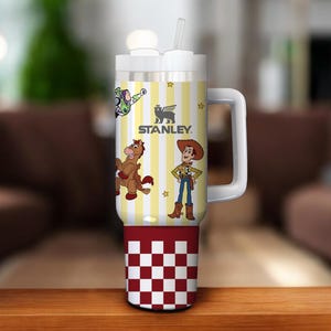 May include: A white and yellow Stanley tumbler with a handle, featuring cartoon characters and the Stanley logo. The bottom section has a red and white checkered pattern. Includes a white lid and straw.