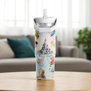 May include: A stainless steel tumbler with a colourful design featuring Disney characters and a castle. The tumbler has a white lid and a straw. The words "Your Name" are printed on the tumbler.