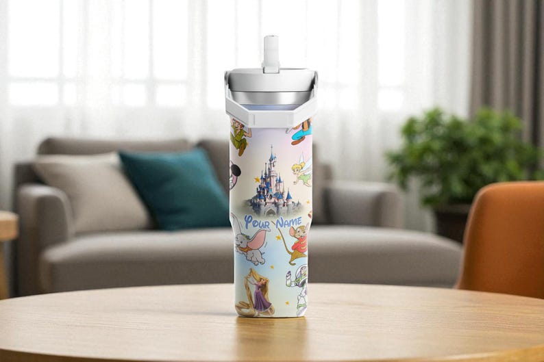 May include: A stainless steel tumbler with a colourful design featuring Disney characters and a castle. The tumbler has a white lid and a straw. The words "Your Name" are printed on the tumbler.