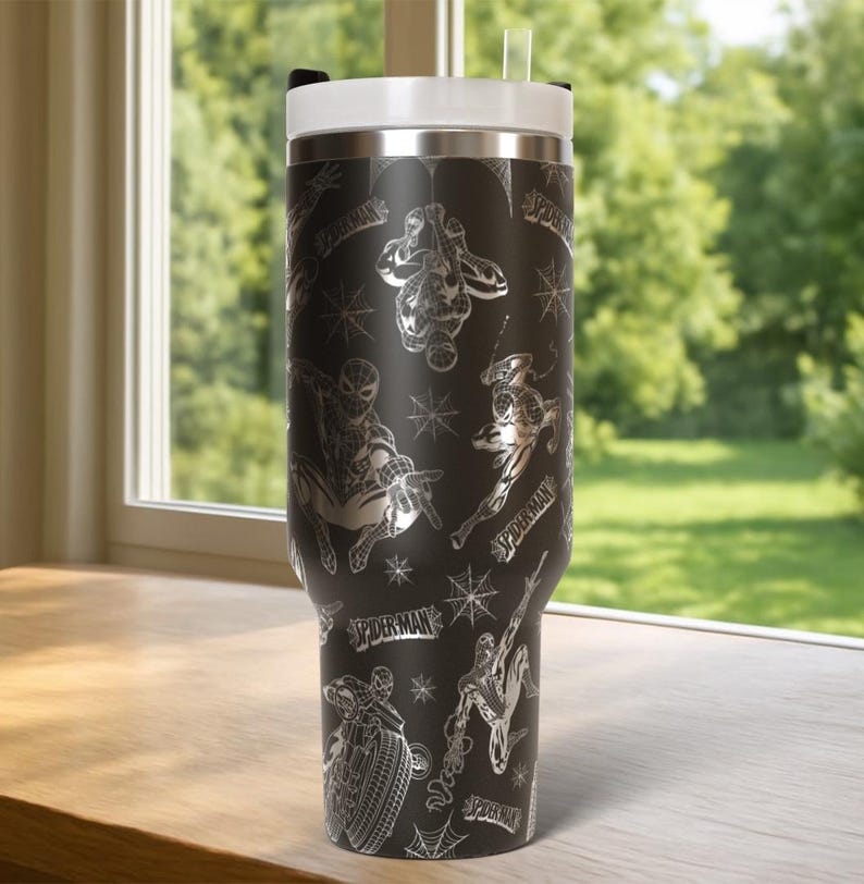 Pu&ograve; includere: Bicchiere nero con coperchio e cannuccia bianchi, con un motivo ripetuto di illustrazioni di Spider-Man e ragnatele. Il bicchiere ha la scritta "SPIDERMAN" in argento. Il bicchiere &egrave; su una superficie di legno.