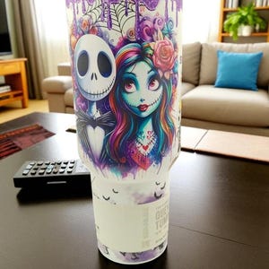 May include: A white tumbler featuring Jack Skellington and Sally from The Nightmare Before Christmas. The design includes a purple glitter top, dripping accents, and a floral arrangement. The tumbler has a white band with text.