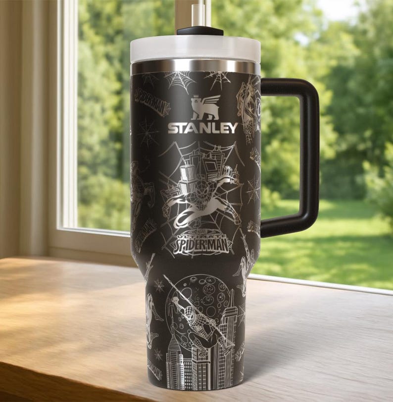 Pu&ograve; includere: Tazza da viaggio Stanley nera con coperchio bianco e manico nero. La tazza presenta un design di Spider-Man con il testo "STANLEY" e "SPIDER-MAN" in argento. Il design include ragnatele, paesaggi urbani e illustrazioni di Spider-Man.