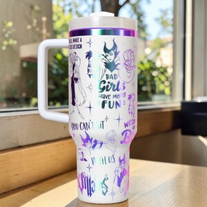 Puede incluir: Vaso t&eacute;rmico blanco con asa, con ilustraciones de villanos de Disney y el texto "BAD Girls HAVE MORE FUN". El vaso tiene una tapa blanca y una banda morada y plateada en la parte superior.