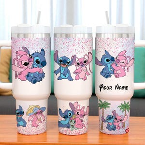 May include: White insulated tumbler with a handle, featuring a cartoon design of a blue and pink alien couple. The design includes the text "Your Name" on one tumbler. Each tumbler has a white lid and a straw.