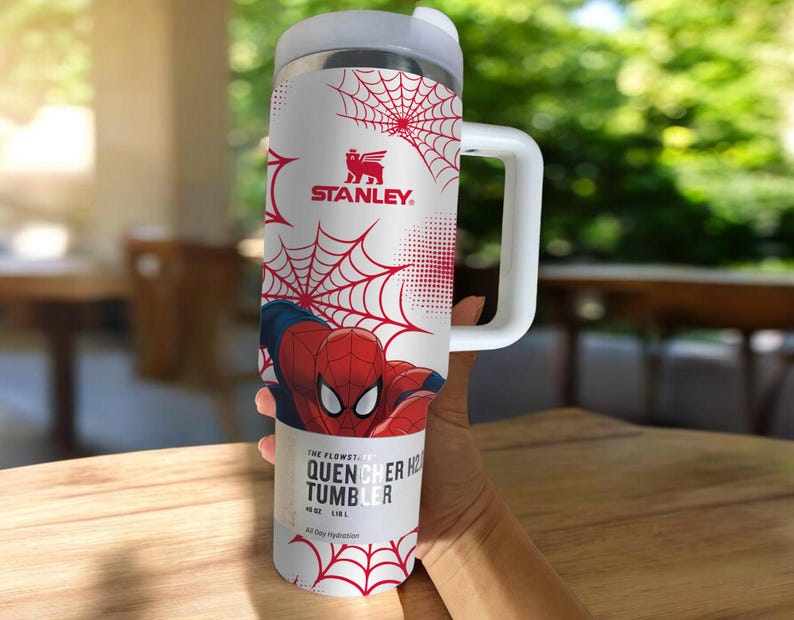 May include: A white Stanley Quencher H2.0 Flowstate tumbler featuring Spider-Man graphics and red spiderwebs. The tumbler has a handle and a white lid. The text on the tumbler reads "THE FLOWSTATE QUENCHER H2.0 TUMBLER" and "40 OZ | 1.18 L".
