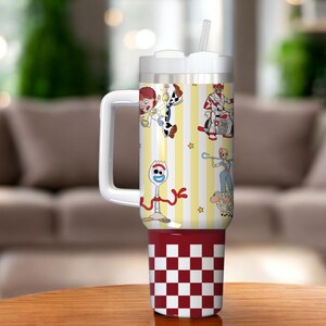 May include: A white and red tumbler with a handle and straw. The tumbler features cartoon characters on a yellow and white striped background. The bottom of the tumbler has a red and white checkered pattern.