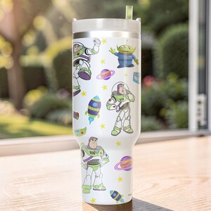 Pu&ograve; includere: Un bicchiere bianco con coperchio argentato e cannuccia verde. Il bicchiere &egrave; decorato con immagini di cartoni animati di Buzz Lightyear, alieni, pianeti e razzi. Stelle gialle sono sparse intorno alle immagini.