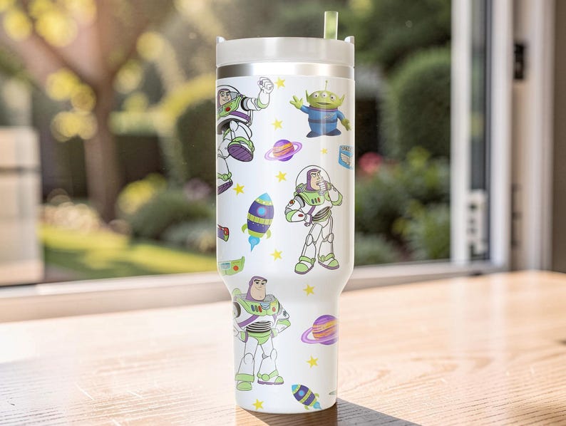 Pu&ograve; includere: Un bicchiere bianco con coperchio argentato e cannuccia verde. Il bicchiere &egrave; decorato con immagini di cartoni animati di Buzz Lightyear, alieni, pianeti e razzi. Stelle gialle sono sparse intorno alle immagini.