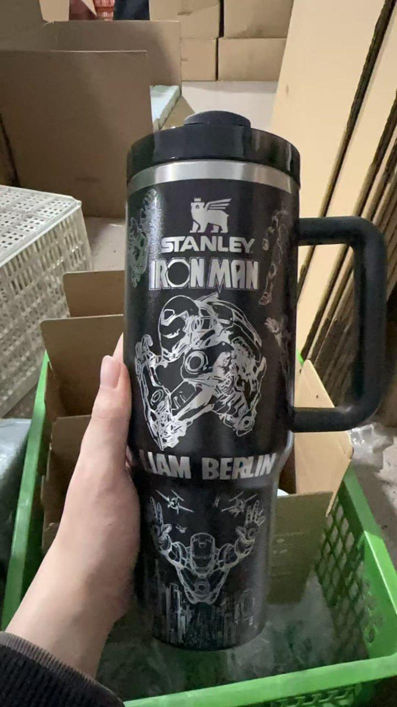 May include: Black Stanley Iron Man travel mug with a black handle and lid. The mug features a silver Iron Man graphic and the text "STANLEY IRON MAN" and "LIAM BERLIN".