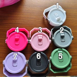 May include: A selection of seven brightly coloured water bottle lids. Each lid is round with a flip-top closure and a handle. The colours are white, grey, pink, hot pink, green, black, and lavender. The lids are made of plastic.