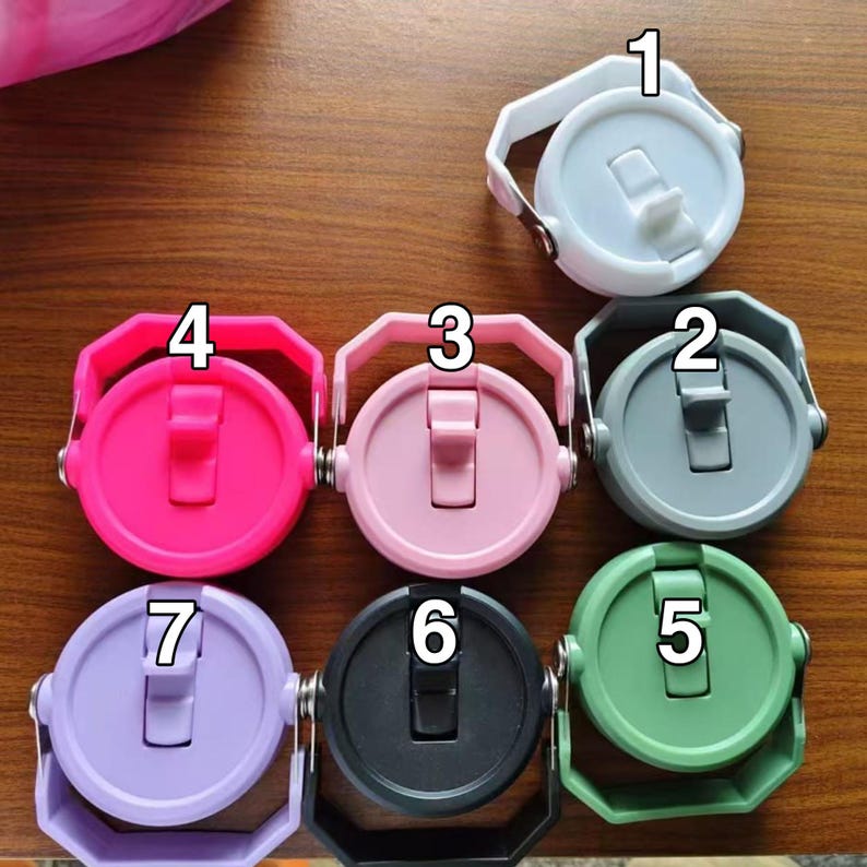 May include: A selection of seven brightly coloured water bottle lids. Each lid is round with a flip-top closure and a handle. The colours are white, grey, pink, hot pink, green, black, and lavender. The lids are made of plastic.