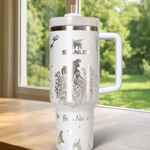 May include: White Stanley tumbler with a handle, lid, and straw. The tumbler features a silver mermaid design, the Stanley logo, and the words "Your Name". Additional silver illustrations include a trident, castle, and stars.