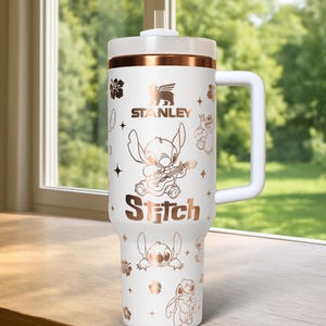 May include: White Stanley tumbler with a handle, featuring a rose gold band and Stitch character graphics. The tumbler includes the Stanley logo and the word "Stitch". The design includes floral and star accents.