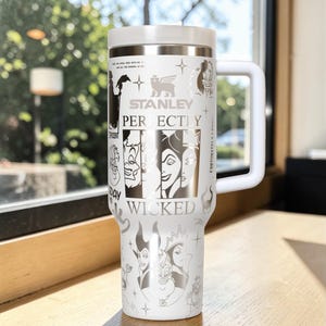 Puede incluir: Un vaso Stanley blanco con asa y tapa blancas. El vaso presenta ilustraciones de villanos de Disney y las palabras "Stanley Perfectly Wicked". El vaso est&aacute; dise&ntilde;ado para mantener las bebidas calientes o fr&iacute;as.