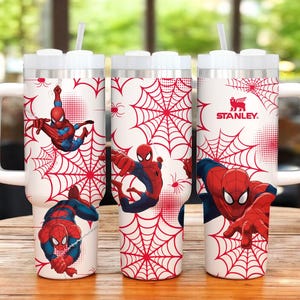 May include: White Stanley tumbler featuring Spider-Man graphics. The design includes red spiderwebs and illustrations of Spider-Man in action. The tumbler has a white handle and lid, and a straw.