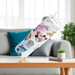 May include: A white water bottle with a cartoon design featuring Mickey and Minnie Mouse, Stitch, and other characters. The bottle has a white lid with a straw and is set on a wooden table. The background includes a grey sofa and a green plant.