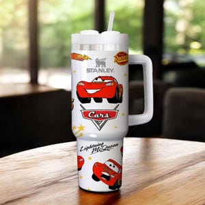 May include: White Stanley tumbler featuring Lightning McQueen from the Cars movie. The tumbler has a white handle, lid, and straw. The design includes the Cars logo and the text "Lightning McQueen".