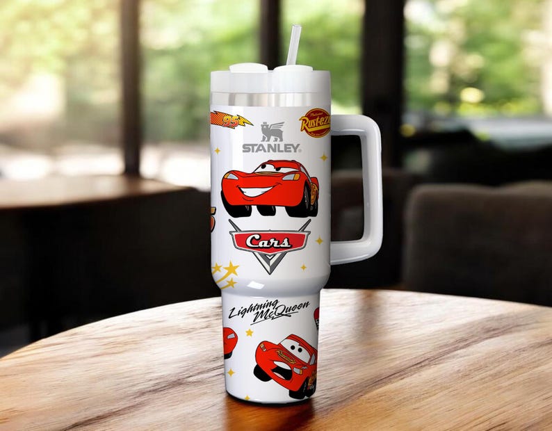 May include: White Stanley tumbler featuring Lightning McQueen from the Cars movie. The tumbler has a white handle, lid, and straw. The design includes the Cars logo and the text "Lightning McQueen".