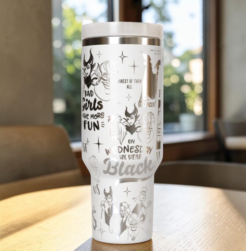 Puede incluir: Vaso t&eacute;rmico blanco con tapa y detalles plateados. El vaso presenta ilustraciones de villanos de Disney y las frases "Bad Girls Have More Fun" y "On Wednesday We Wear Black."