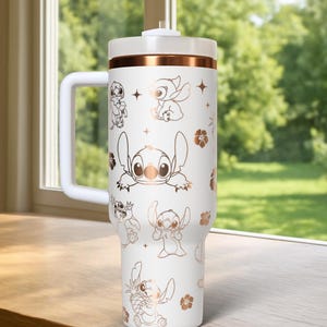 May include: White tumbler with a handle, featuring a copper-colored band and lid. The tumbler is adorned with copper-colored illustrations of the character Stitch from Lilo & Stitch, along with floral and star accents. The tumbler has a white handle.