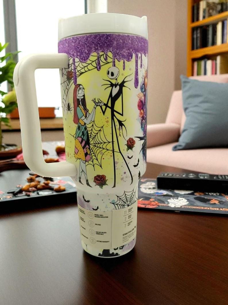 May include: A large white travel mug with a handle, featuring a colorful design of Jack Skellington and Sally from The Nightmare Before Christmas. The mug has a white lid and a purple glitter drip design at the top.