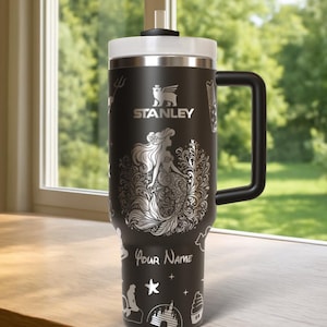 May include: Black Stanley tumbler with a white lid and handle. The tumbler features a silver mermaid design with the text "Your Name". Additional silver illustrations include a trident, castle, and starfish.