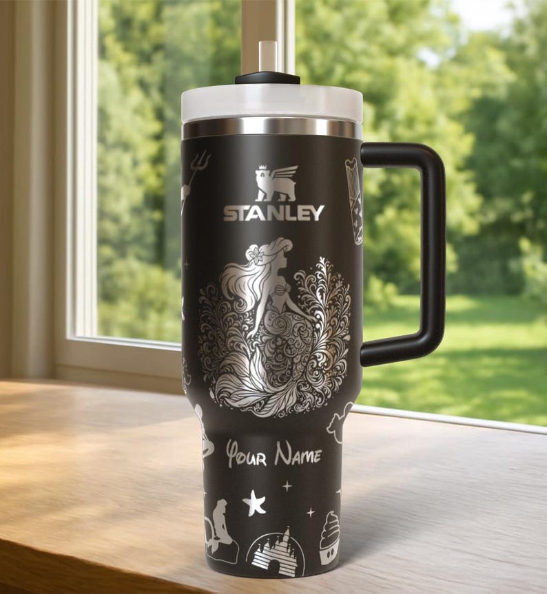 May include: Black Stanley tumbler with a white lid and handle. The tumbler features a silver mermaid design with the text "Your Name". Additional silver illustrations include a trident, castle, and starfish.
