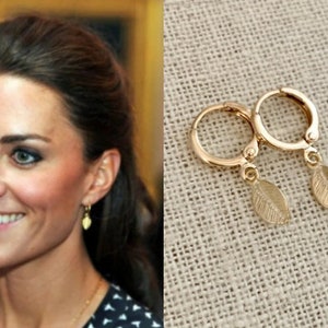 May include: A pair of gold hoop earrings with a small leaf charm dangling from each hoop.