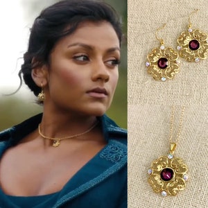 May include: A set of gold filigree jewelry with a purple gemstone in the center of each piece. The set includes a necklace, earrings, and a choker.