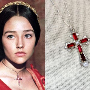 May include: A silver cross pendant with red gemstone accents and a central pearl. The necklace is displayed on a light-colored surface. The image also shows a woman wearing the necklace.