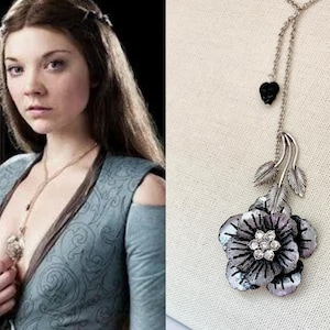 May include: A silver necklace with a black heart charm and a silver flower pendant with rhinestones. The flower has a textured, almost metallic finish.