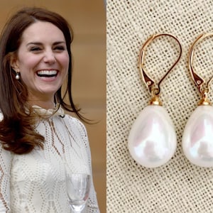 May include: A pair of gold-colored drop earrings with large, pear-shaped white pearls. The earrings have a lever-back closure. The image also shows a woman wearing a similar pair of pearl earrings.
