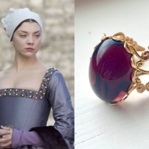 May include: A gold ring with a large, oval-shaped, dark purple gemstone set in a delicate, ornate design.